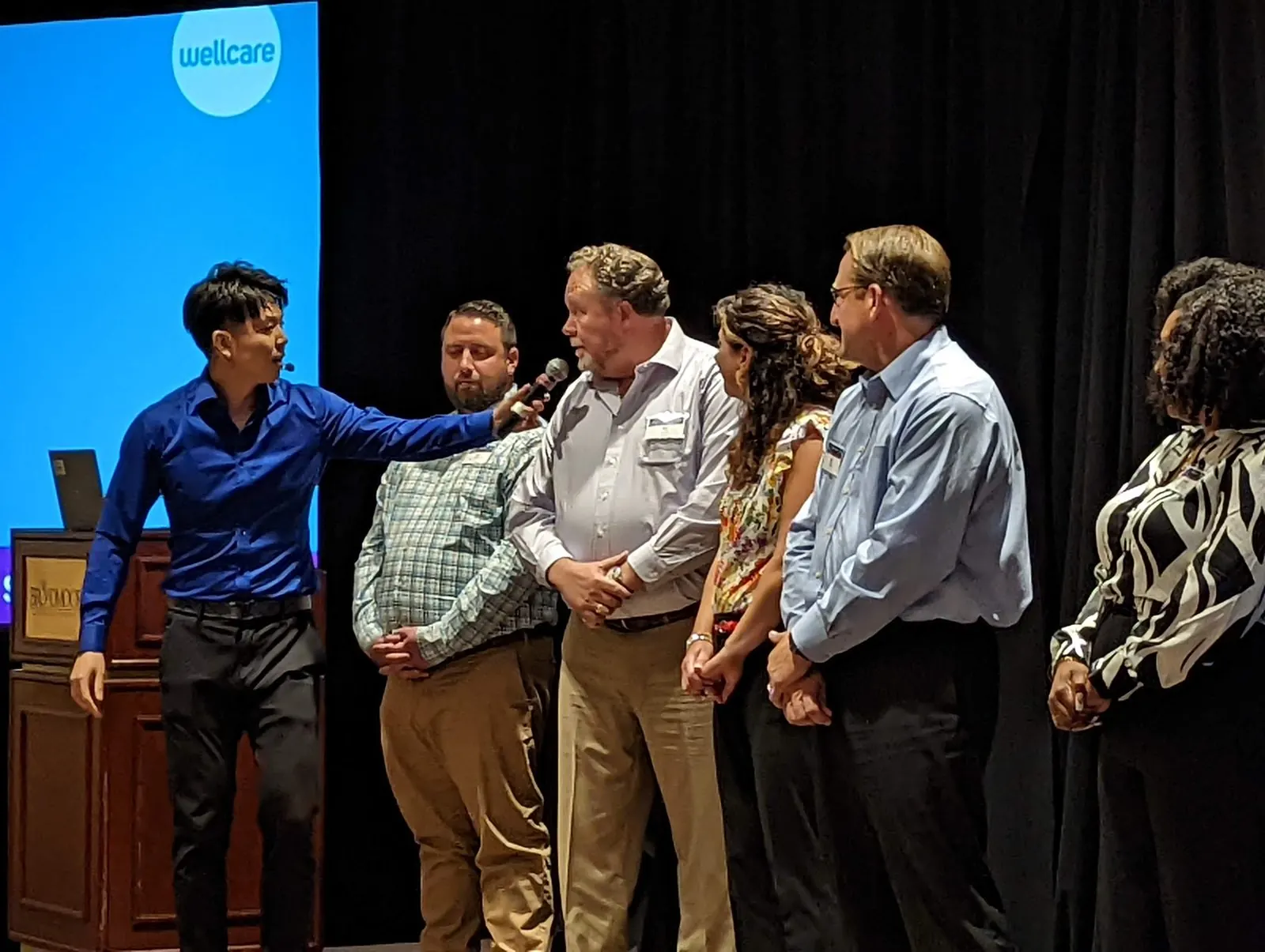 Johnny Wu on stage with volunteers at a sales conference