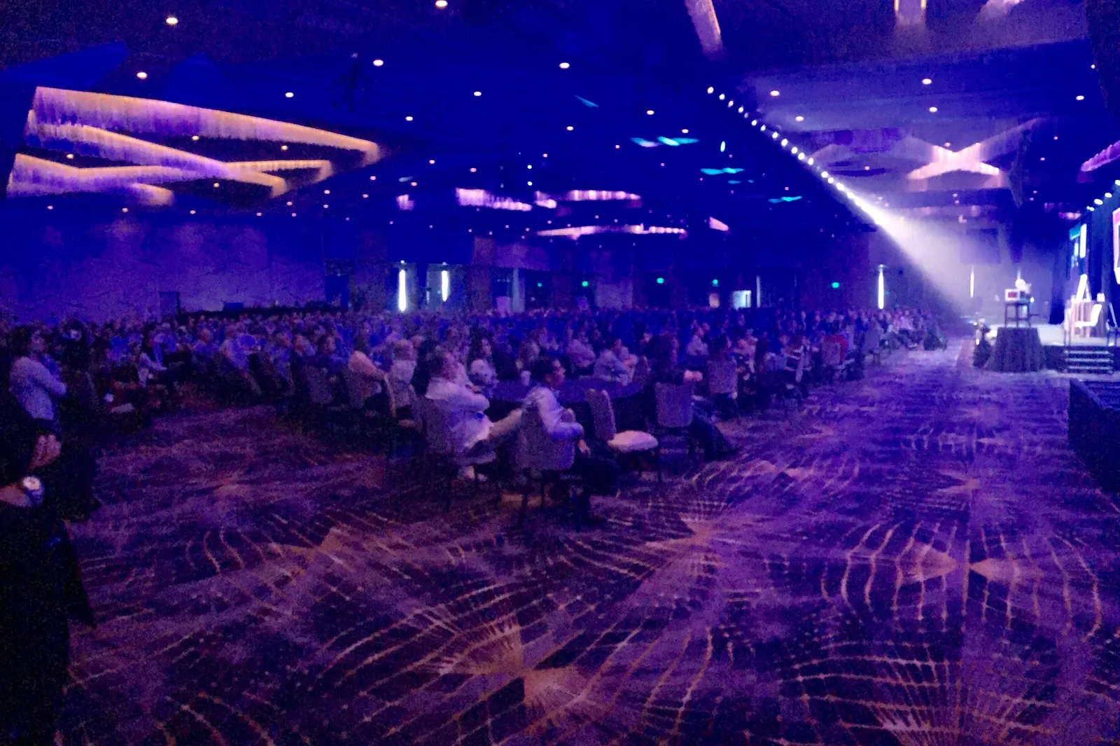 A large conference hall lit purple with the audience seated at tables for the show