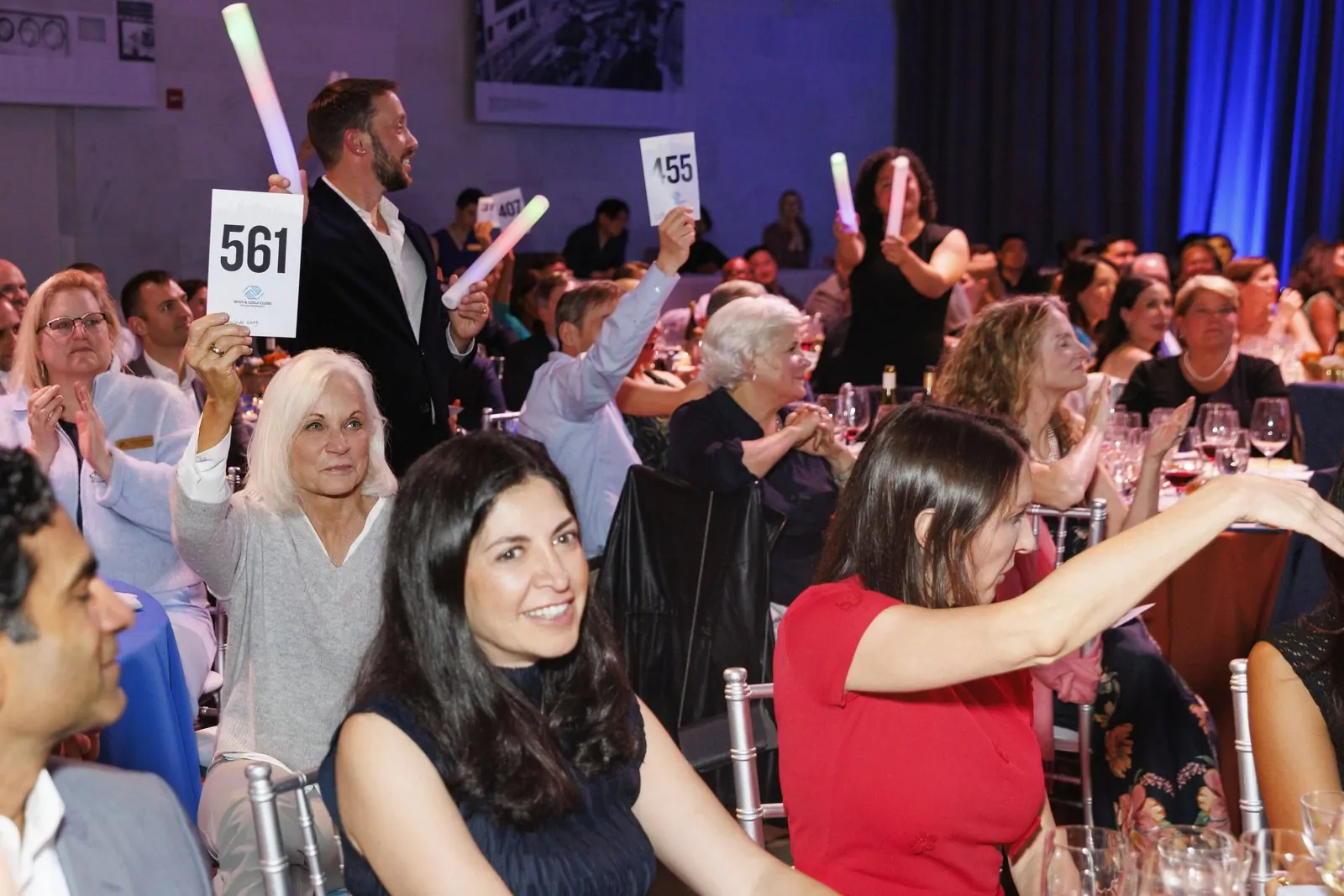 A full gala room raising paddles and glow sticks during a live fundraising moment
